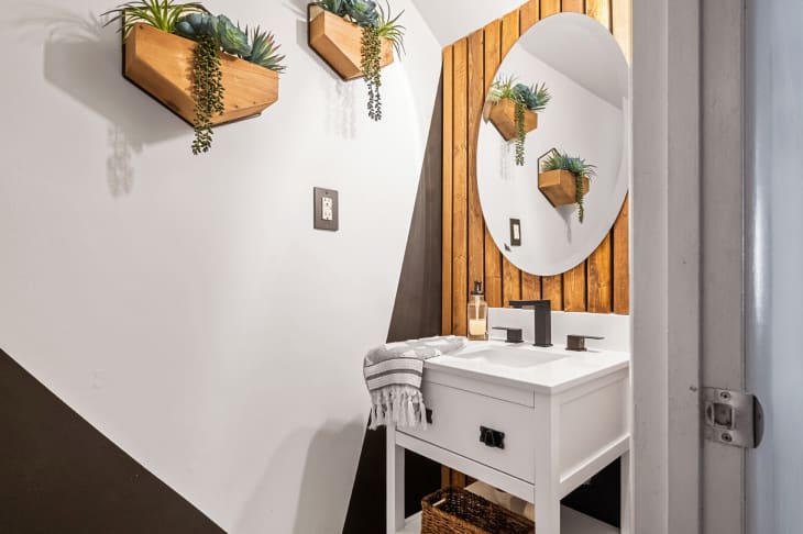 Bathroom with white and brown graphic wall, wood slat accents, and wooden wall planters with plants