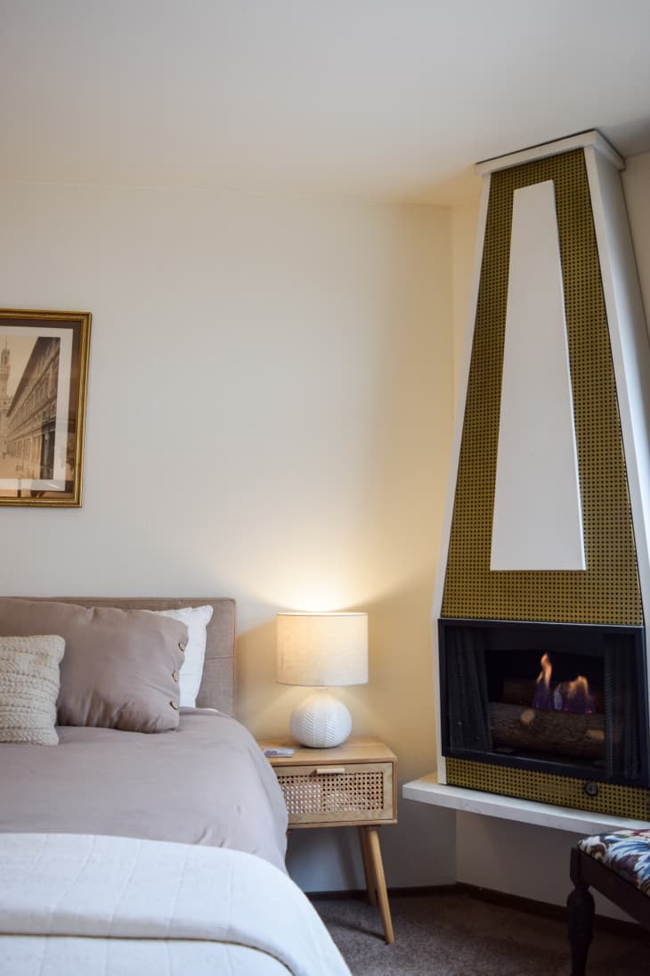 A fireplace next to a bed with derogative pillows