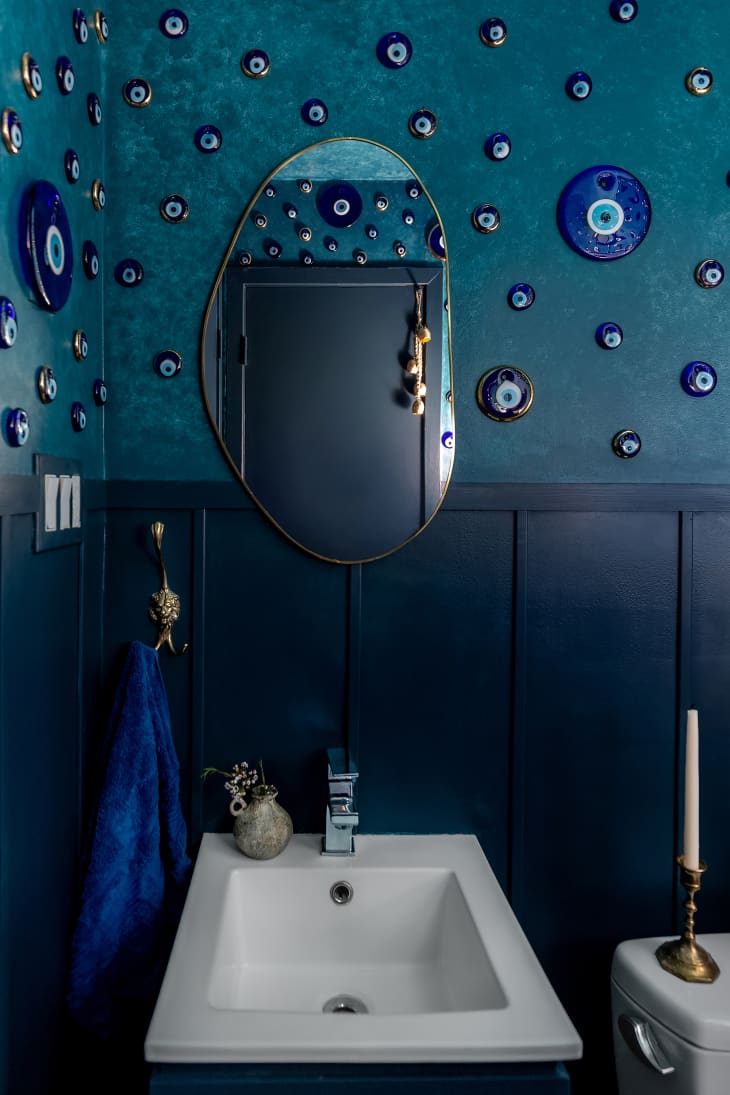 Blue wainscoting in monochromatic bathroom with eye paintings on the wall.