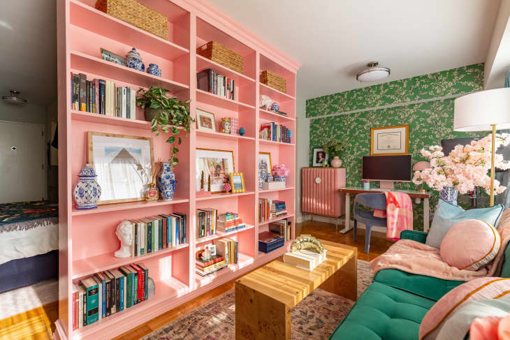 A living room with a green fabric couch across from a pink bookcase and gallery wall