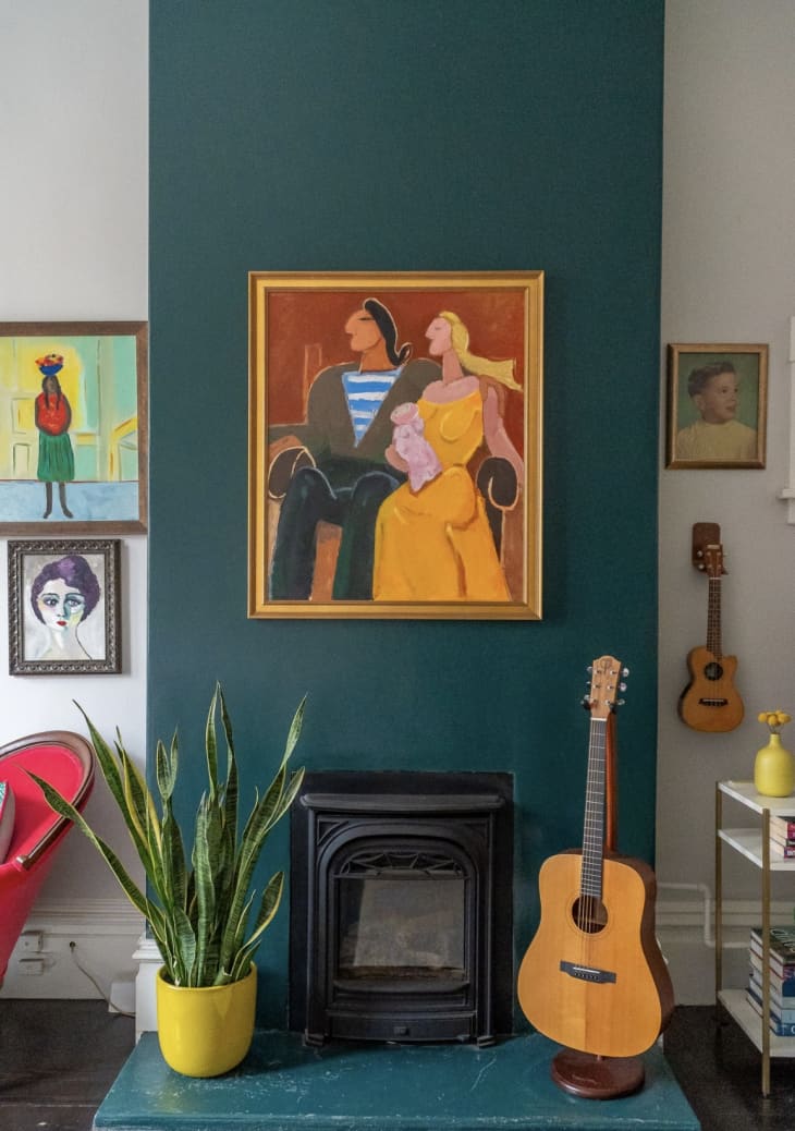 Dark teal accent wall with small fireplace, art, snake plant, and guitar