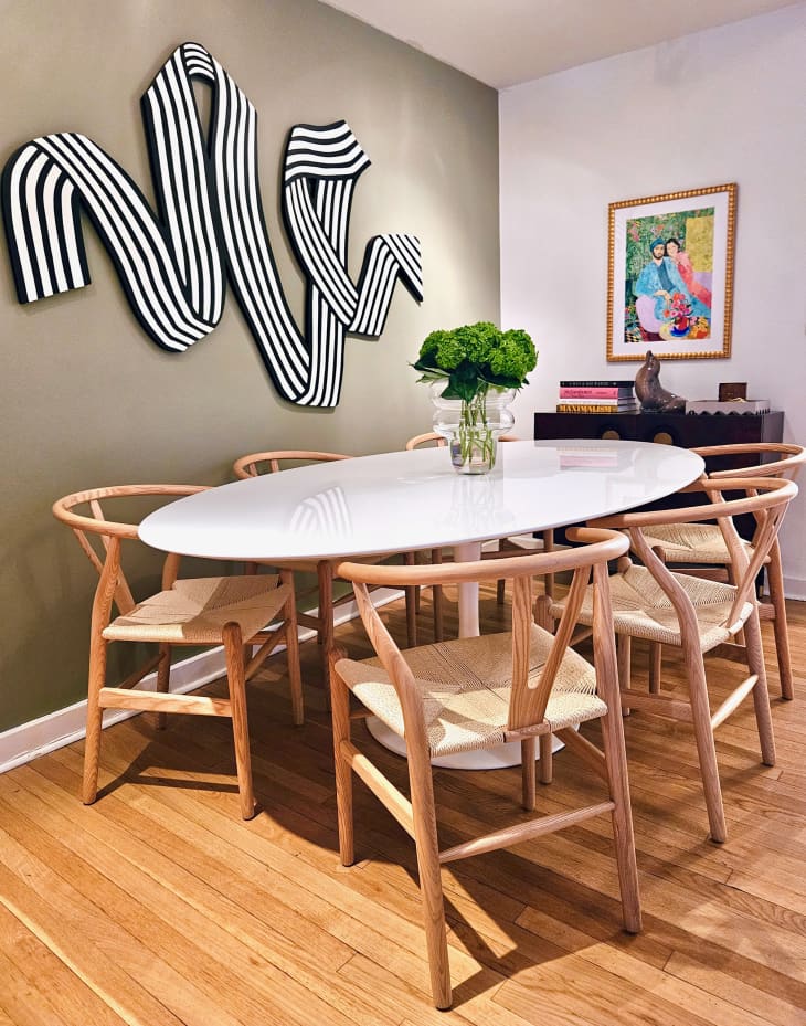 Dining room with one gray accent wall with statement art piece, oval white table with wood and rattan chairs