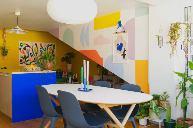 White dining room with colorful mural wall and view into yellow living area
