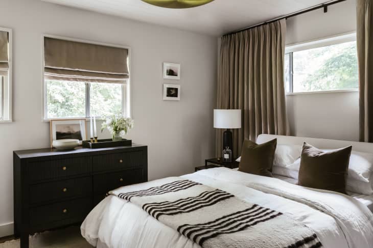 White wood plank ceiling, white linens on bed, black and white striped throw blanket, beige curtains, black modern dresser