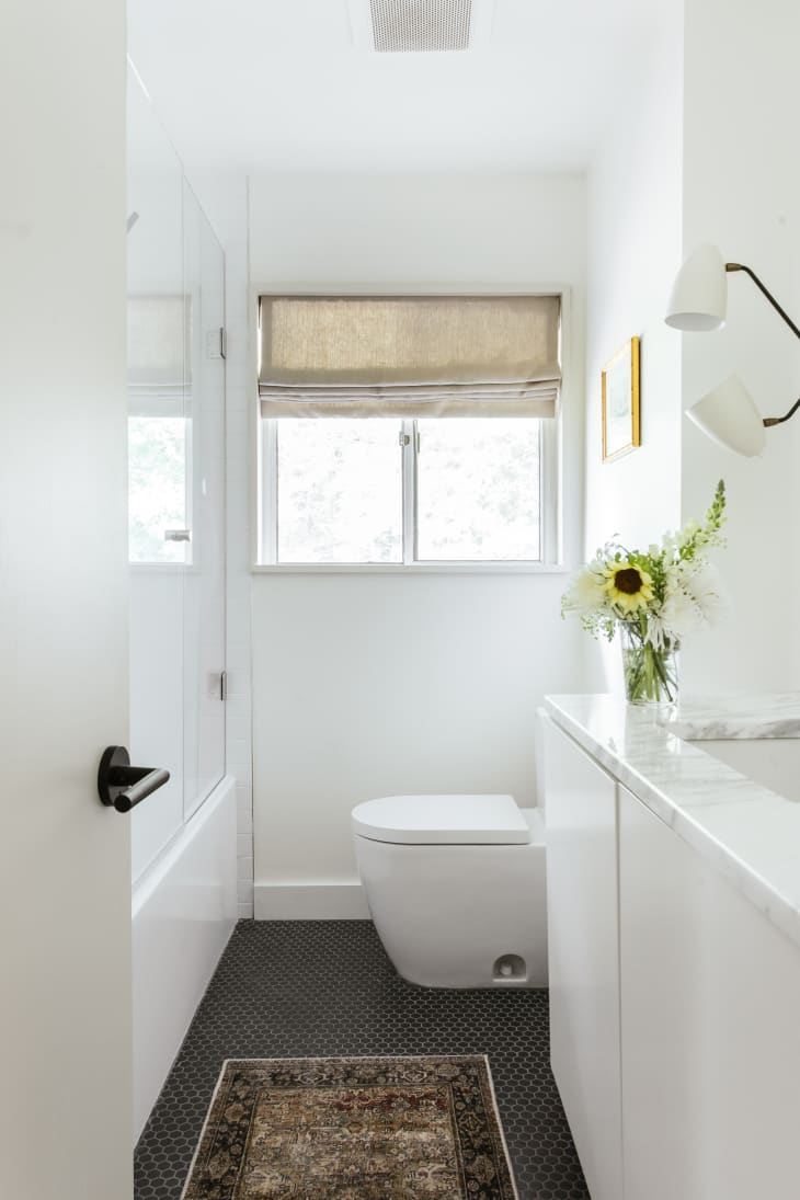 Beige roman style curtains, white cabinets, dark penny tile floor, modern toilet, half glass shower wall