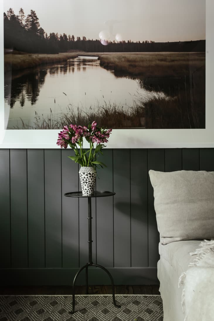 dark green tongue and groove wall paneling, pond landscape with train in background, small metal side table, small vase with flowers