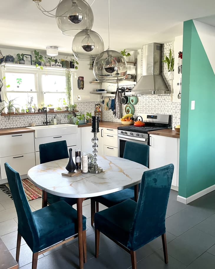 white kitchen with lots of plants, bold color paint details, and dining table with blue chairs