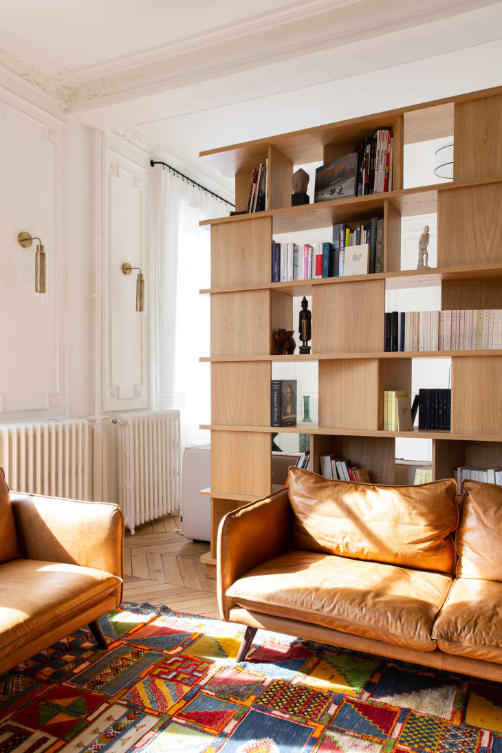 Bookshelf in living room with colorful rug and cognac leather seating.