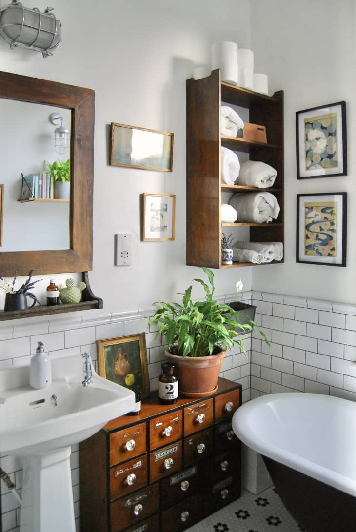 White bathroom with wooden storage shelf, mirror and cabinets in a white tiled bathroom.