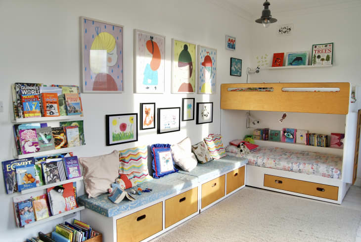 A child's bedroom with a bench and wooden bunk bed with decorative items on the wall.