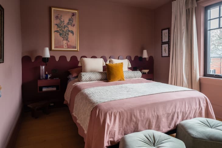 A bed with a burgundy built-in headboard and an orange decorative pillow.
