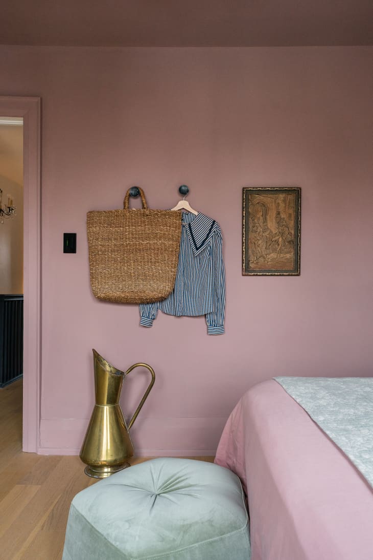 Woven bag and shirt on a hook with pink walls and framed art.