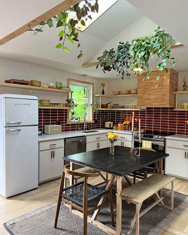 white kitchen with deep red tile backsplash and skylights with lots of plants