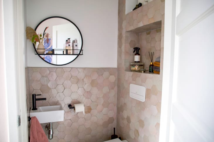 Round mirror seen in view of bathroom with neutral hexagonal tiles.