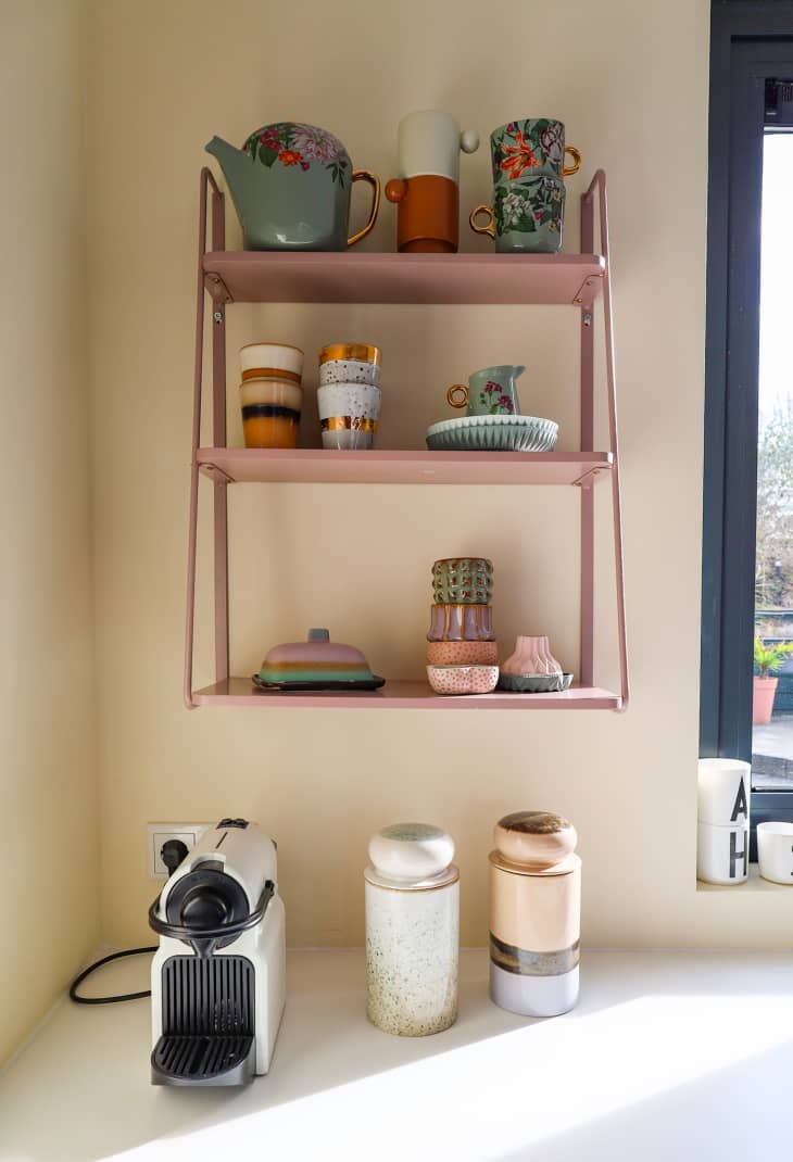 Pink wall shelves hold drinkware in neutral kitchen.