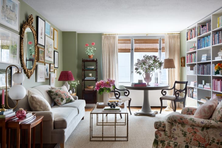 Gallery wall above couch, floor to ceiling color coded bookshelf, floral arm chair, round white table, vintage chairs and side tables