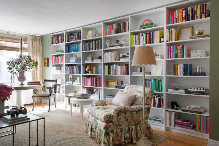 floor to ceiling color coded book shelf wall, floral chair with skirt
