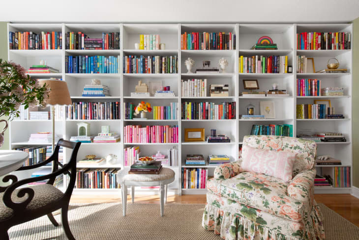 floor to ceiling color coded book shelf wall, floral chair with skirt