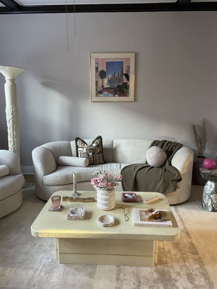 Rounded edge modern white coffee table, boucle white sofa, beige rug, dark green throw
