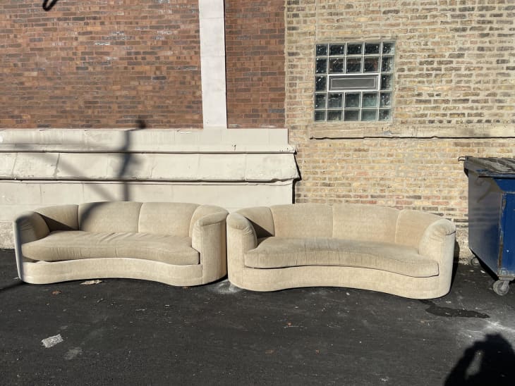 2 beige curved boucle sofas in alley in front of brick walls