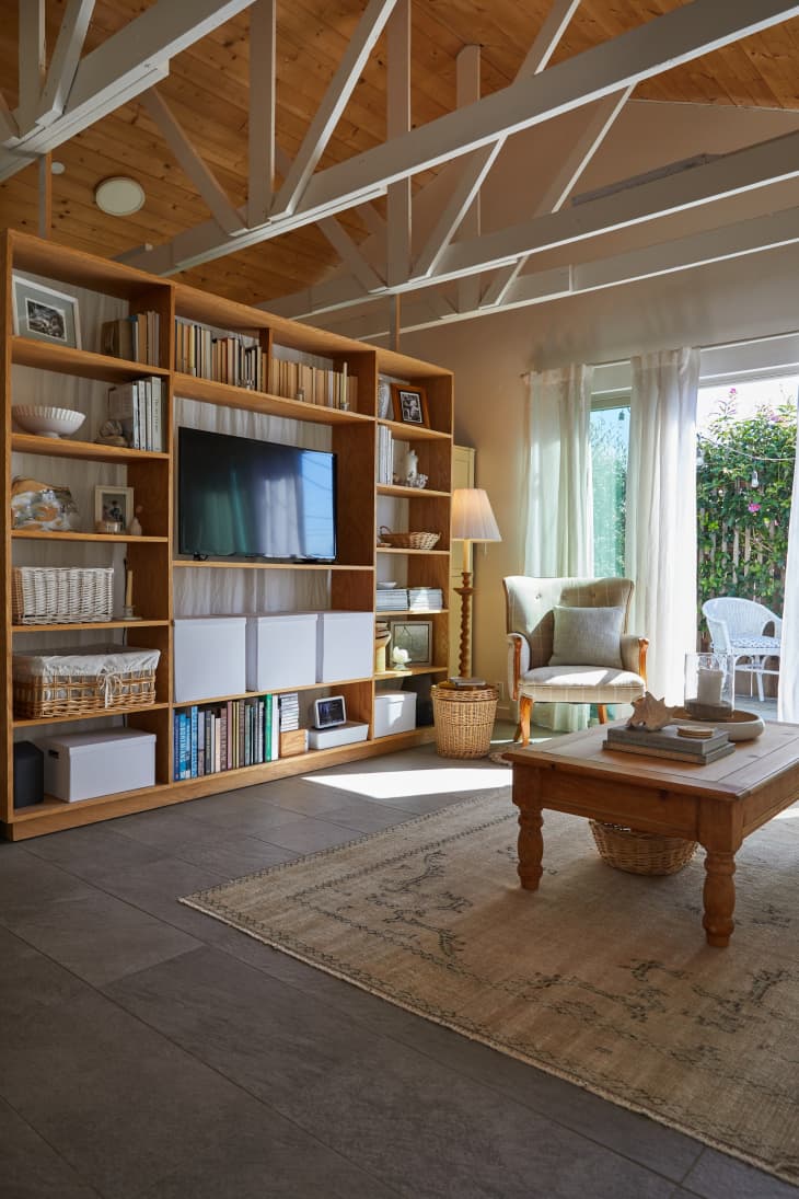 A large media bookcase with TV books and decorative items divides the bedroom from the living room area.