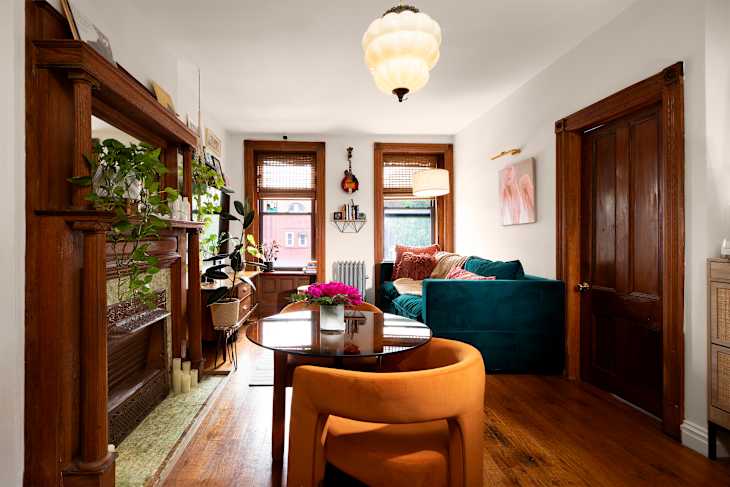 Cozy living room with teal sofa, orange chairs, wooden accents, plants, and a round dining table with flowers.
