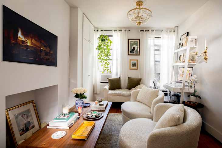 Cozy living room with a chandelier, two round chairs, a white sofa, and a wooden coffee table adorned with books and decor.