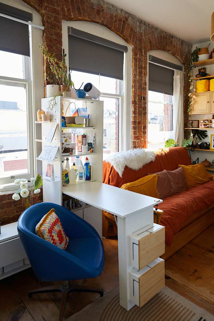 Small white desk in living room with burnt orange sofa.