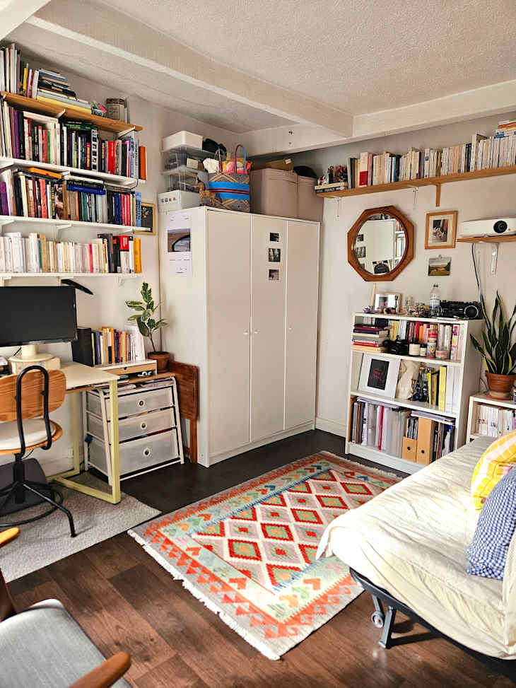 Cozy room with a desk, bookshelves, a large rug with geometric patterns, and a foldable sofa.