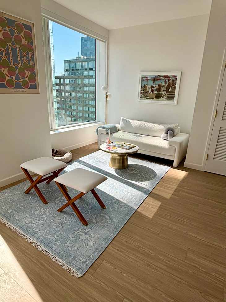 Bright living room with a white sofa, two wooden stools, a round coffee table, and a light blue rug.
