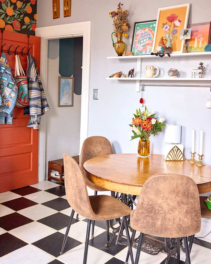 Cozy dining area with a round wooden table, brown chairs, floral centerpiece, and colorful wall art.