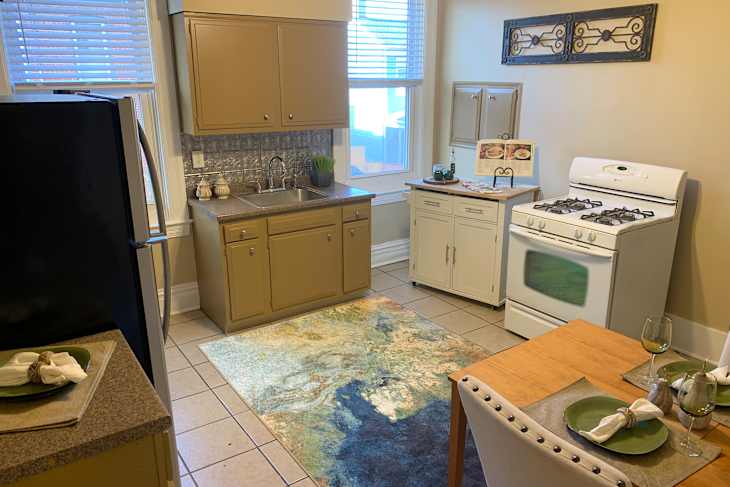 Cozy kitchen with beige cabinets, a white stove, a colorful rug, and a small dining table set for two.