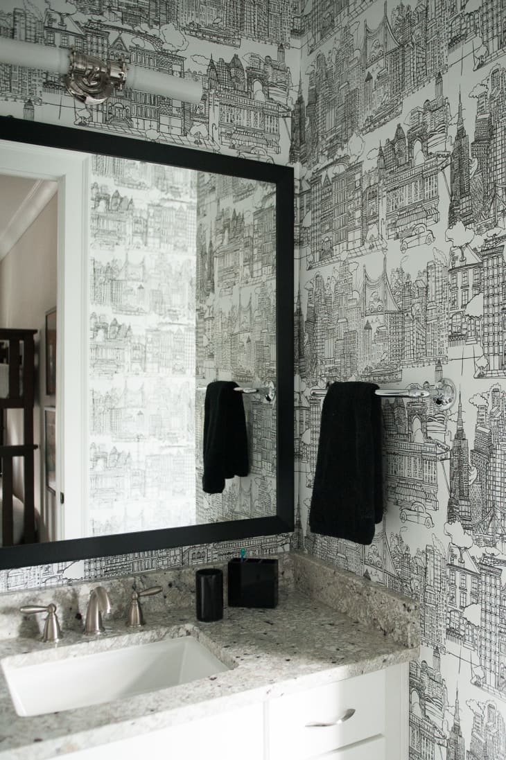 Powder room with graphic black and white wallpaper and black frame mirror