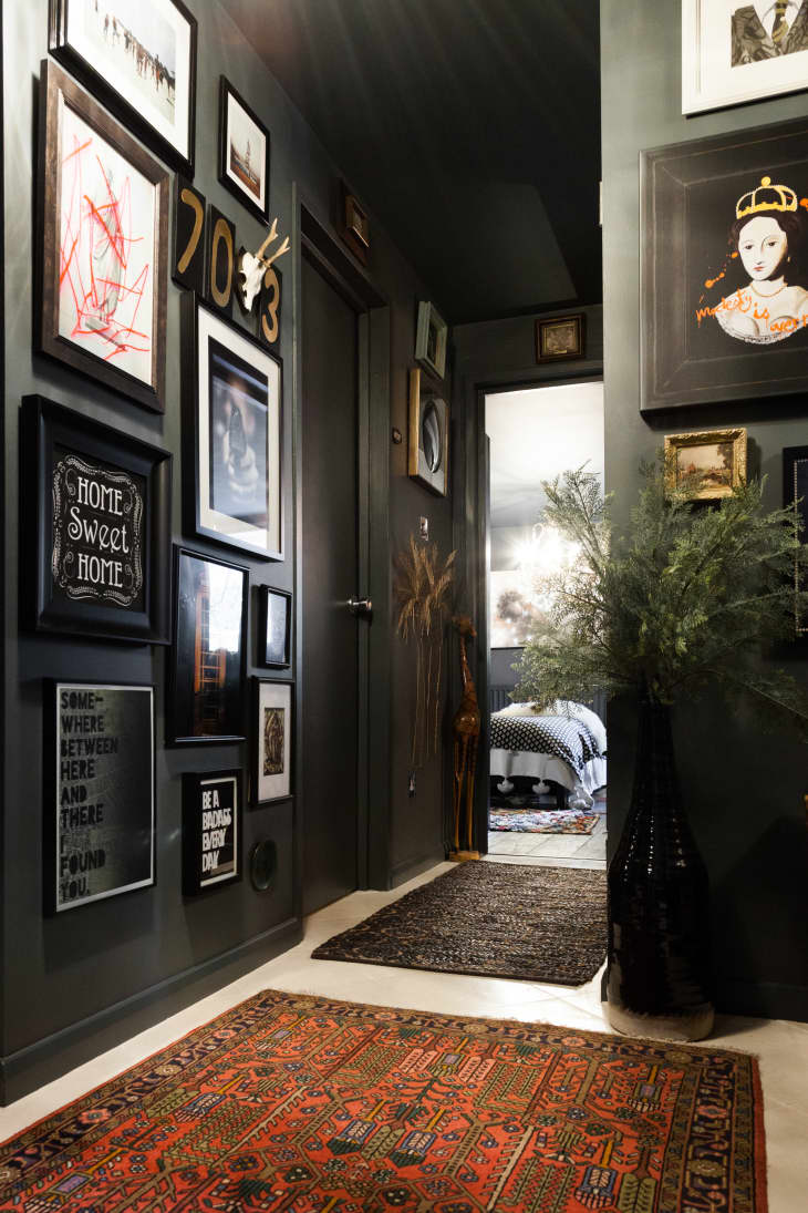 An apartment entryway with the walls painted black and lots of framed artwork on the walls