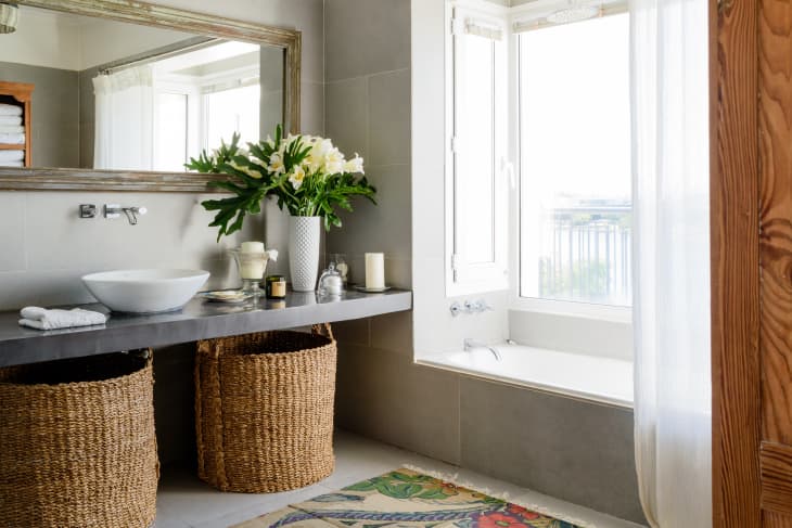 A bathroom vanity with round weave laundry baskets placed underneath and a bathtub beside it