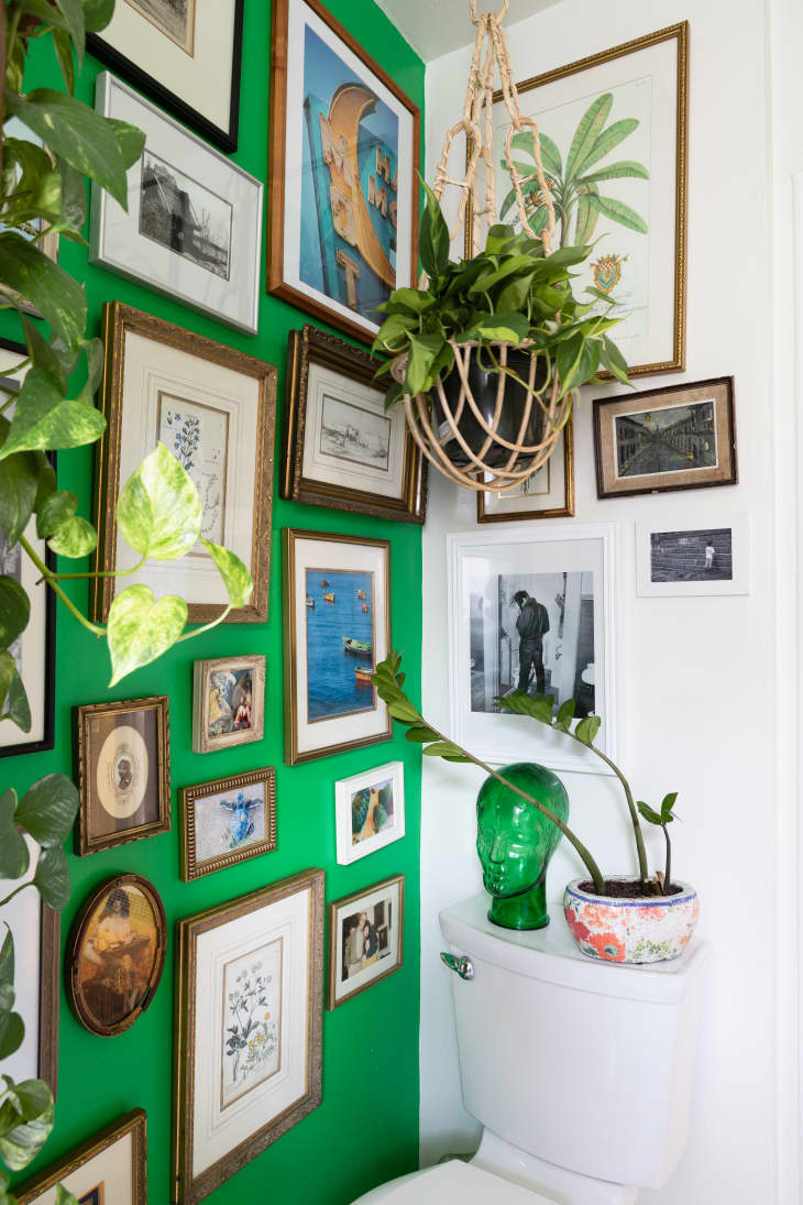 A small bathroom with green walls features a floor-to-ceiling gallery wall.