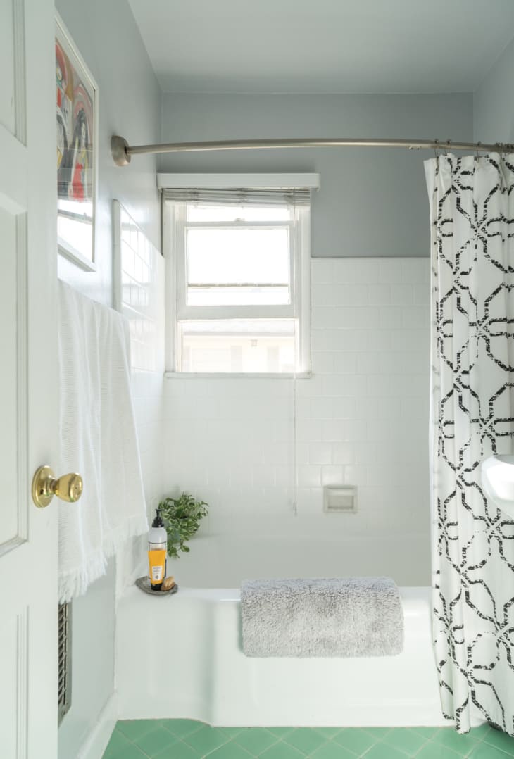 A bathroom with green tile flooring, white shower tiling and gray walls.