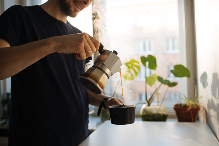 Man pouring coffee out of moka pot in sunny kitchen with plants
