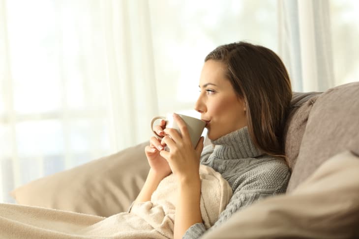 Woman sitting on couch with blanket sipping hot coffee