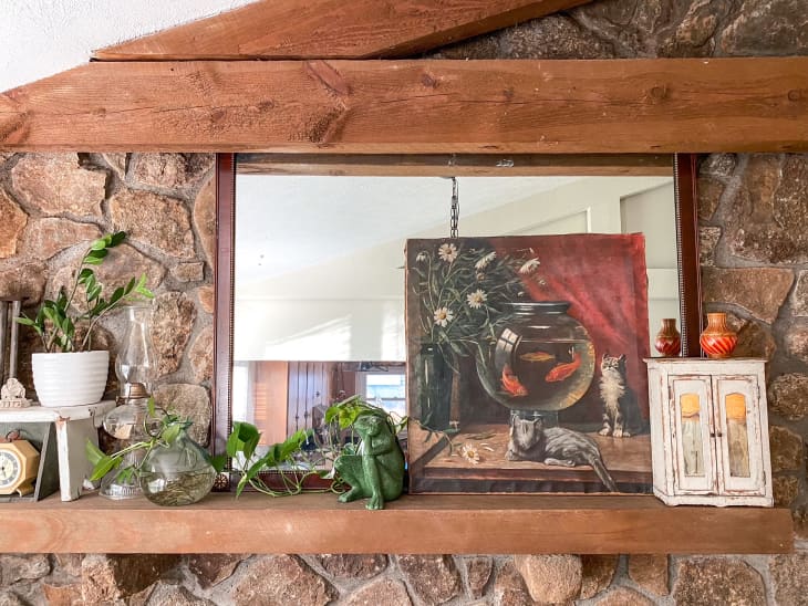 Stone wall with wooden shelf featuring plants and painting