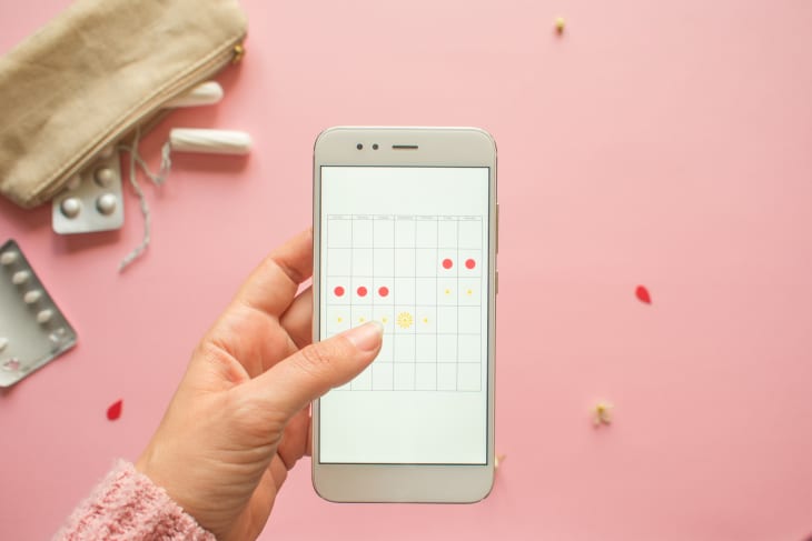 Woman holding phone using period-tracking app on pink background