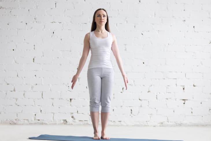 Woman doing yoga mountain pose standing on yoga mat in white room