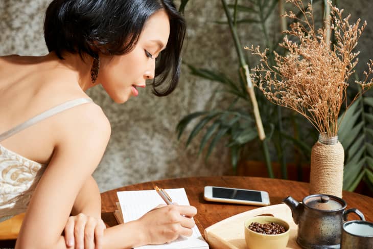 Woman sitting at table with phone and coffee journaling