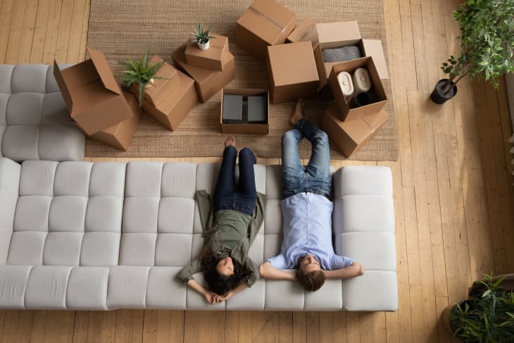 Couple laying on couch with unpacked cardboard boxes on floor