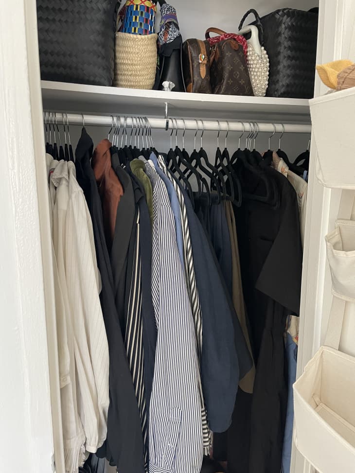 view into closet with clothes hanging, purses and baskets of accessories on shelf above