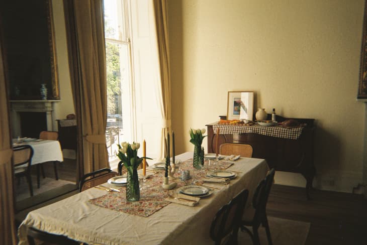 Dinner party table with tablecloth, nice place settings, candles, vase of tulips. windows behind