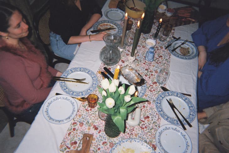 Dinner party table with tablecloth, nice place settings, lit candles, vase of tulips. somewhat overhead shot of people at the table after eating