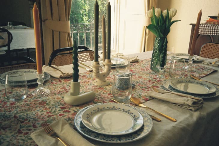 Dinner party table with tablecloth, nice place settings, candles, vase of tulips. windows behind