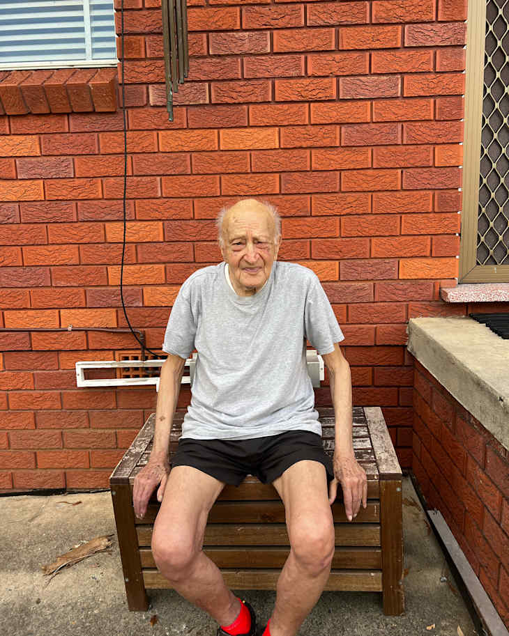 Elderly man sitting on storage bench.