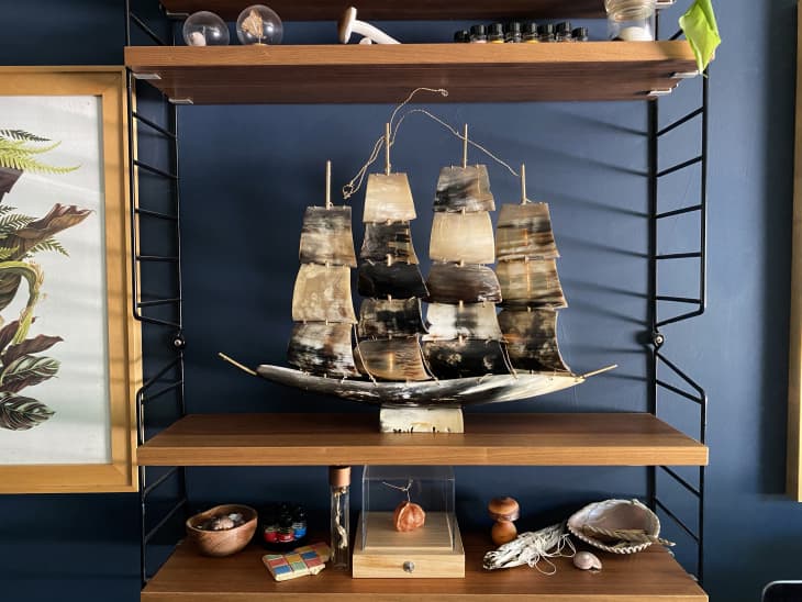 A bull horn sail ship model sits on a modern wooden shelf in a blue room